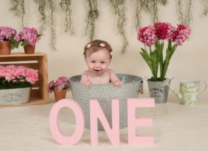 One year old girl sitting in a metal bath tub with O N E in front