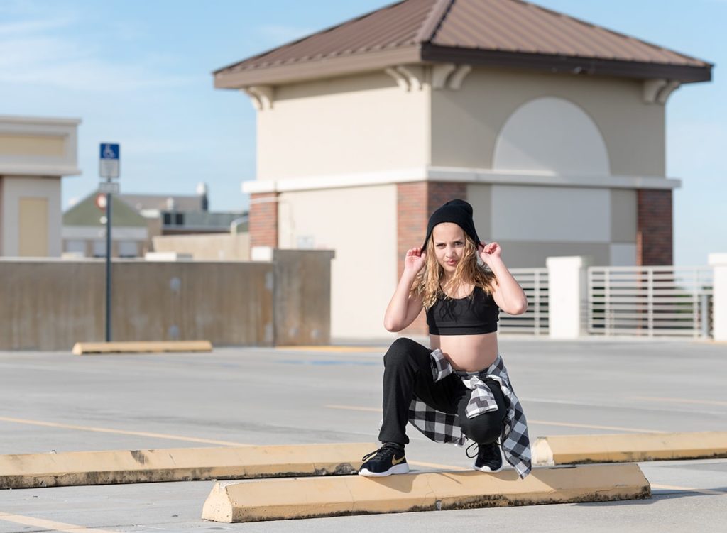 Tween girl crouching on a parking garage concrete bar
