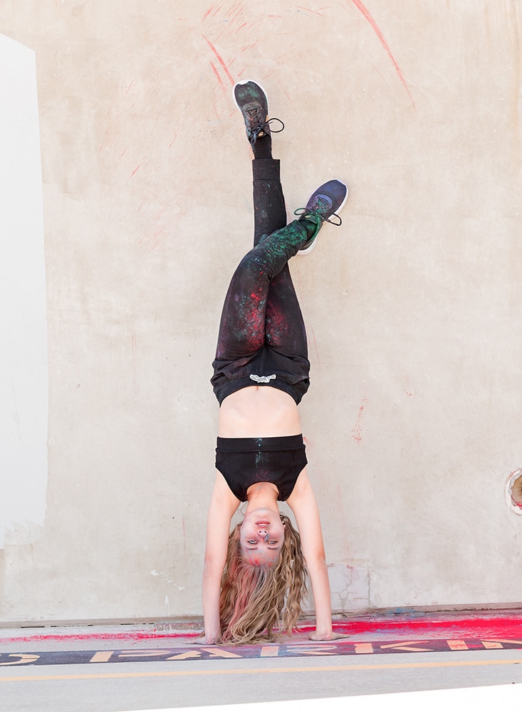 Tween dancer standing on her hands leaning against a parking garage wall
