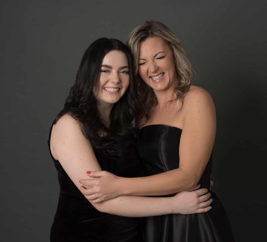 Mom and daughter wearing black ball gowns and hugging while laughing