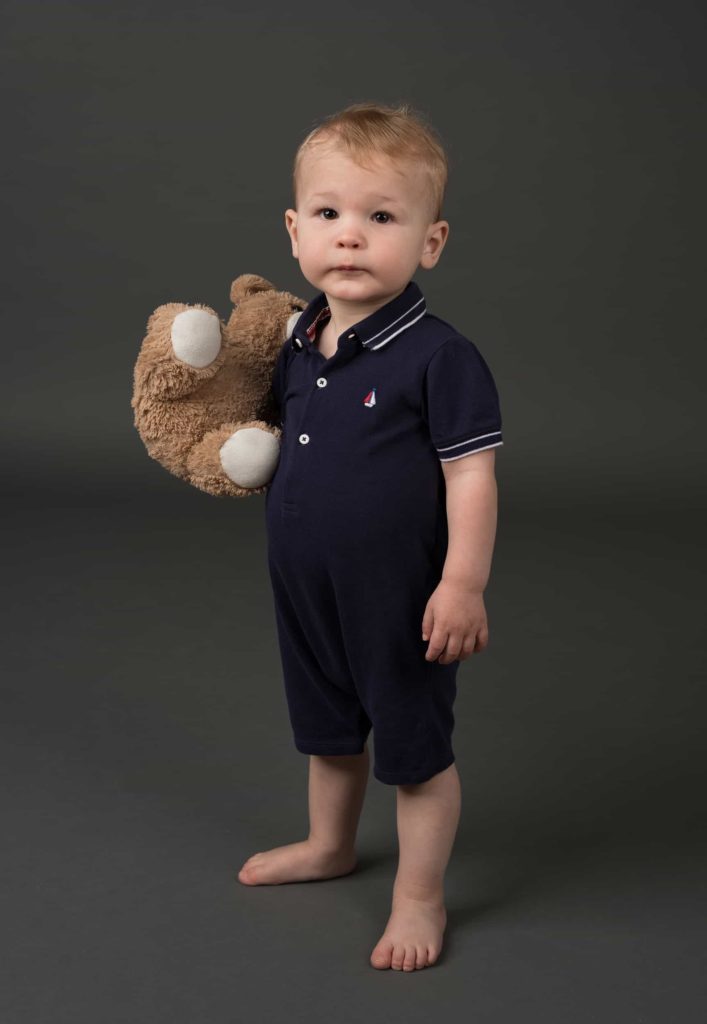 Baby in a navy onesie holding a bear
