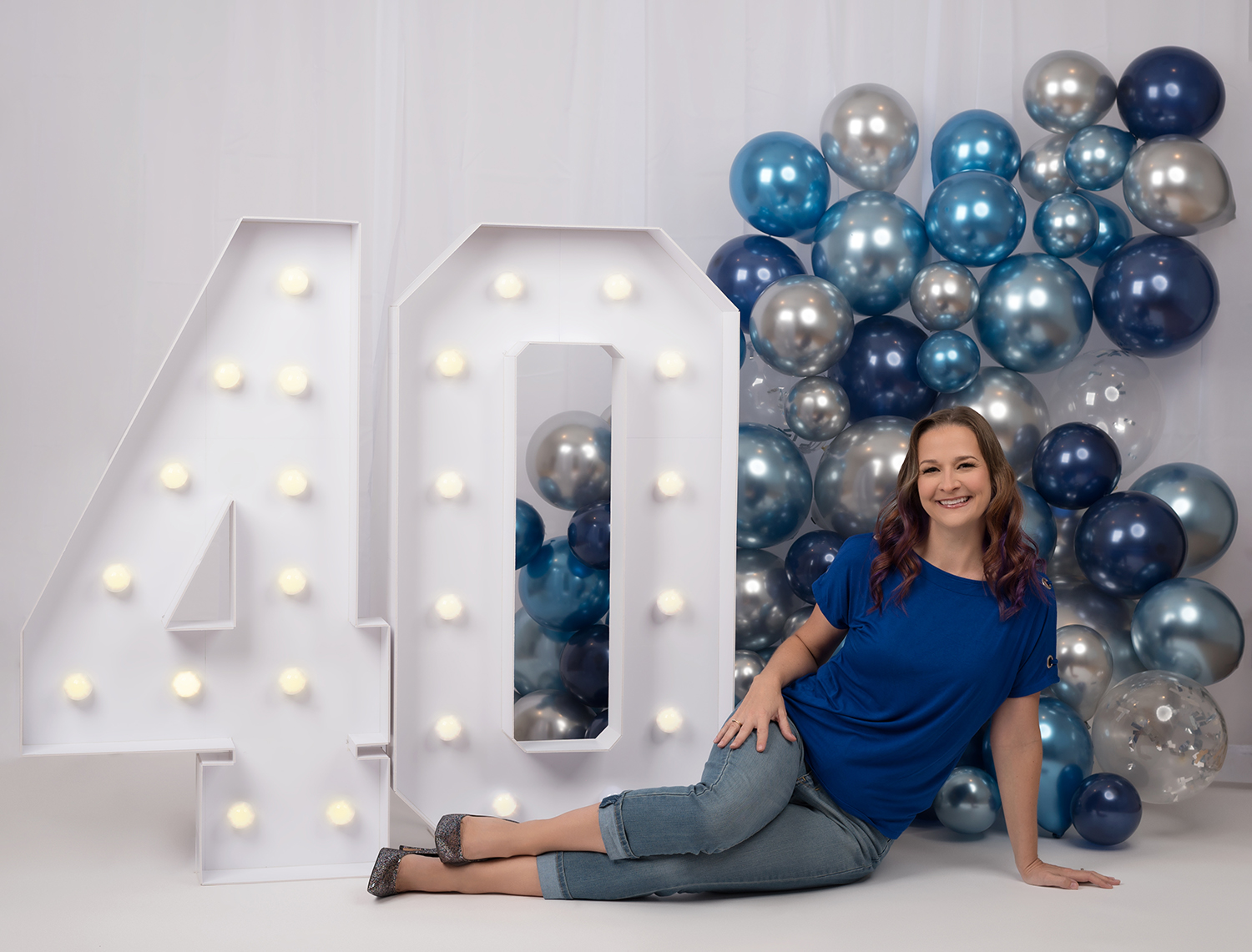 Woman sitting on floor next to large 40 sign and balloons